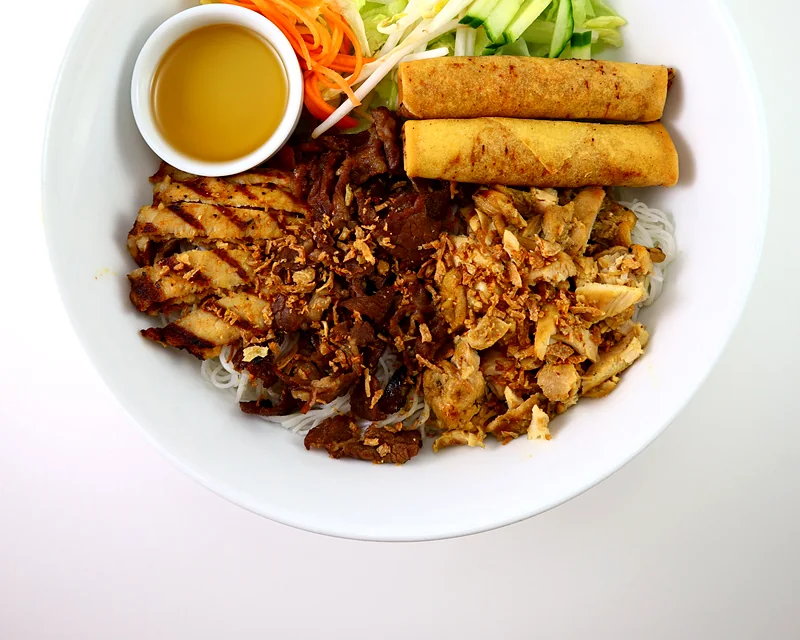 Vermicelli bowl with lemongrass chicken, BBQ pork and bulgogi beef, spring rolls, lettuce, cucumber, carrot and fish sauce